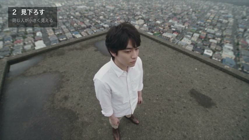 同じ男性を頭の上から見下ろす。背景は屋上の床と街
