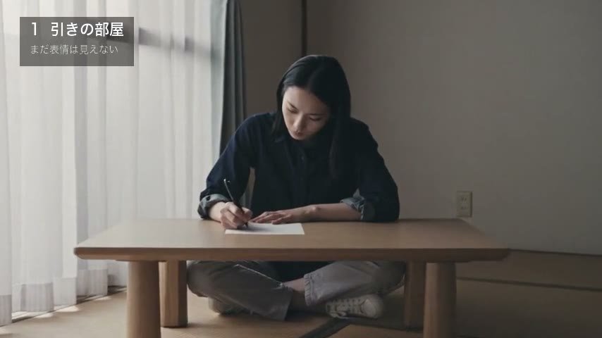 部屋の低い机で手紙を書く女性。顔は小さい