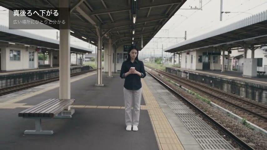 屋根とベンチのあるホームに、女性が小さく立つ